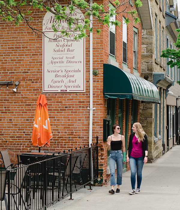 Two women walk on a sidewalk as they talk and smile.