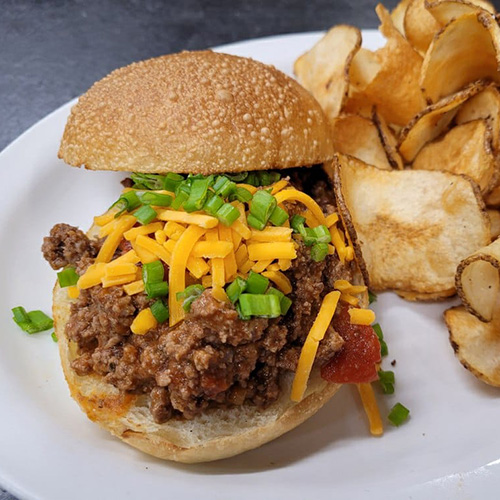 A hamburger with shredded cheese on top, and a side of fries.