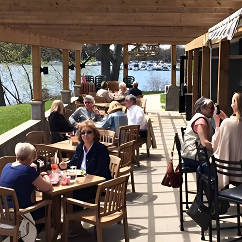 People sit on a busy patio that's on the water.