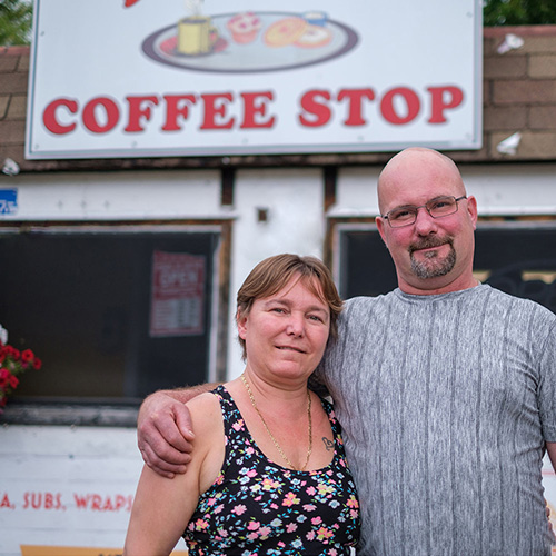 Two people stand in front of a sign that reads "Coffee Stop"