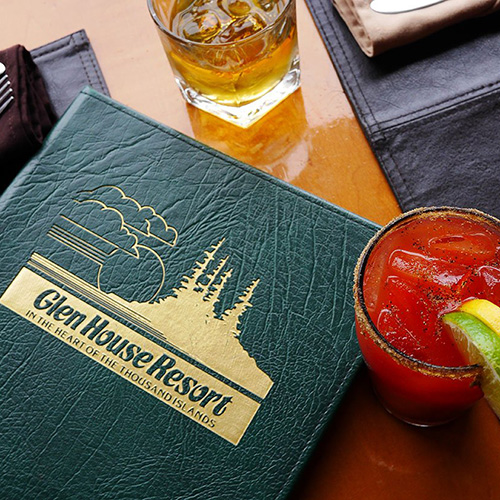 A green menu for Glen House Resort sits beside a cocktail on a table.