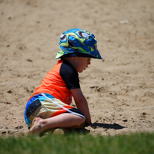 A young child wearing a sunhat plays in the sand.