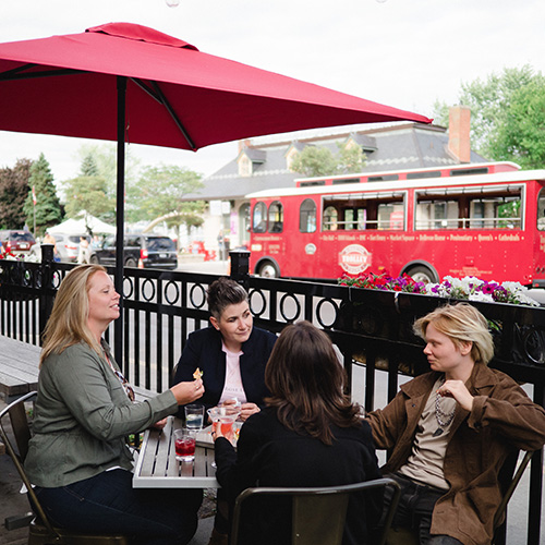 A group of four people sit on a patio with a red trolley in the background.