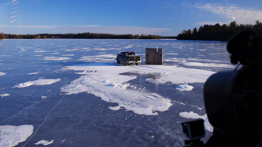 An ice fishing hut and a truck on a frozen lake.